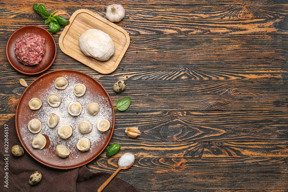 Plate with uncooked dumplings and ingredients on wooden background