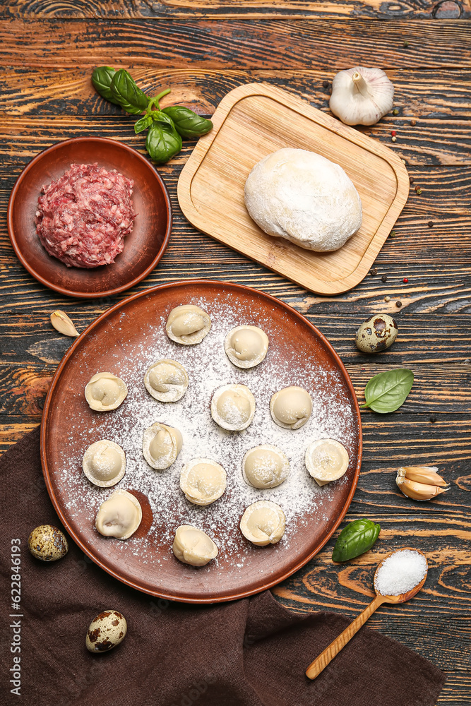 Plate with uncooked dumplings and ingredients on wooden background