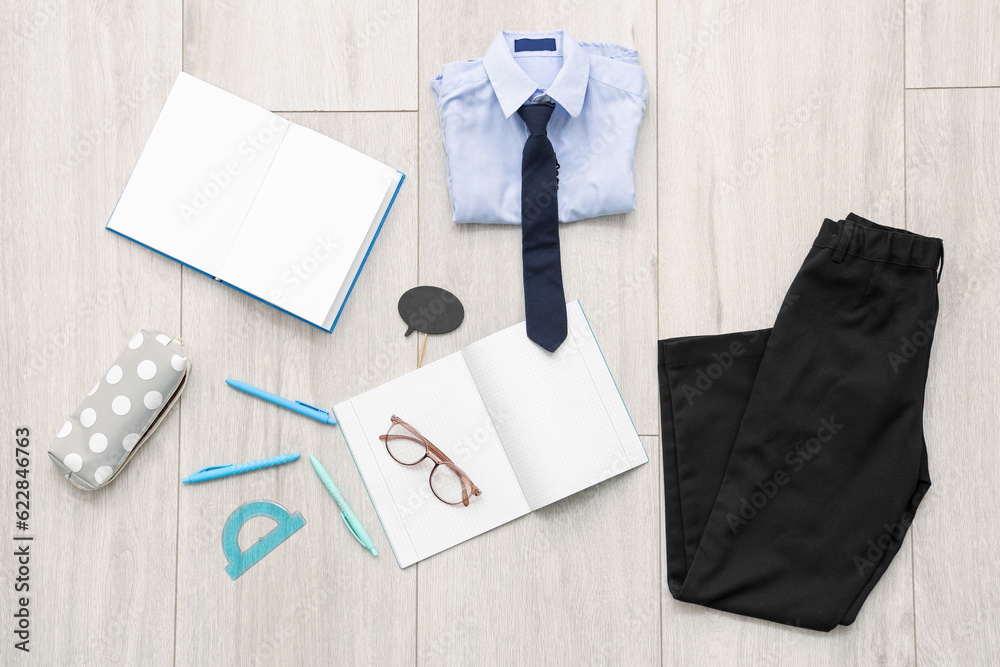 Composition with stylish school uniform, eyeglasses and stationery on wooden background