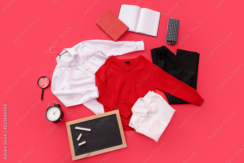 Composition with stylish school uniform, chalkboard, alarm clock and stationery on red background