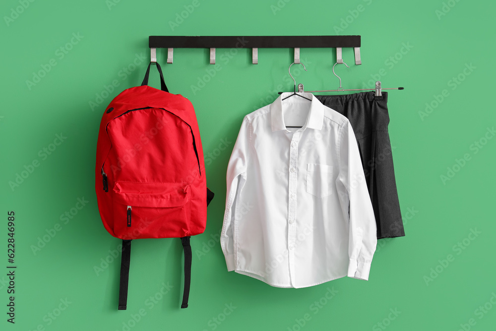 Stylish school uniform and backpack hanging on rack near green wall in room