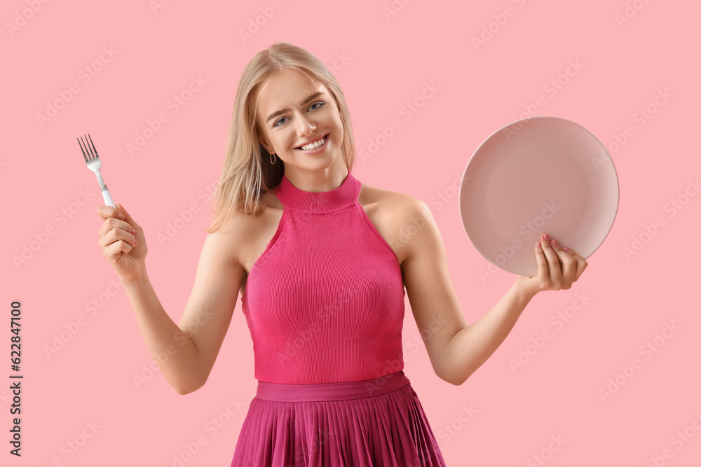 Young woman with fork and plate on pink background