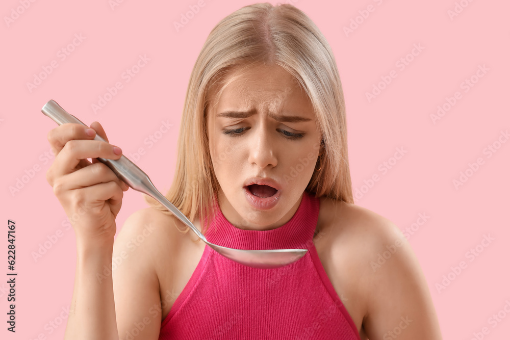 Upset young woman with ladle on pink background, closeup