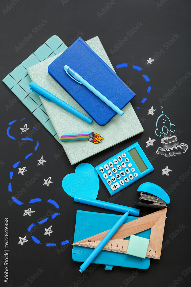 Creative composition with drawn rocket and different stationery on black chalkboard