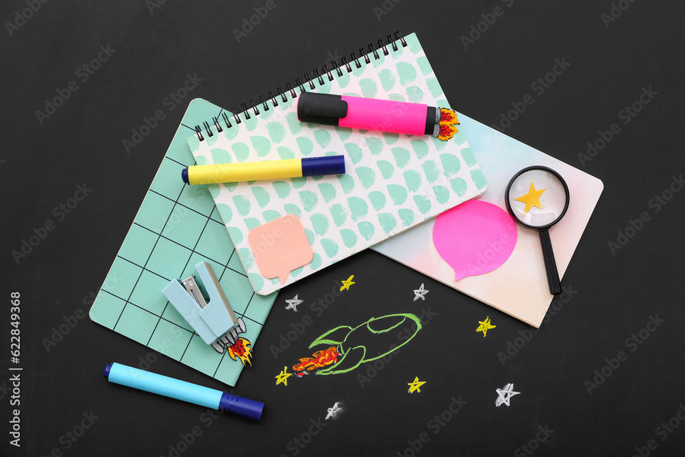 Creative composition with rockets, magnifier and different stationery on black chalkboard