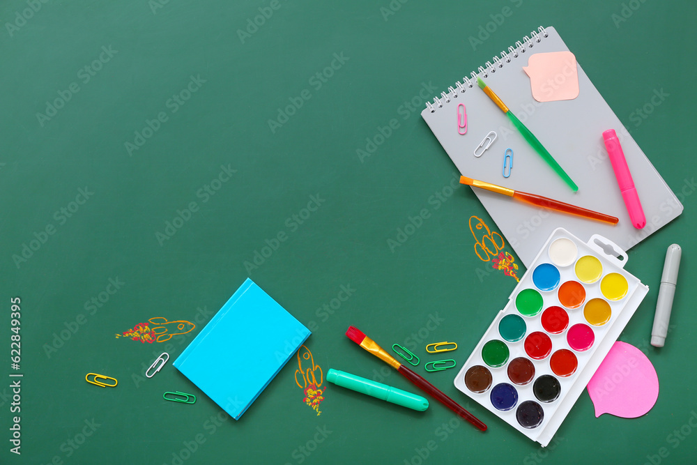 Creative composition with drawn rockets and different stationery on green chalkboard