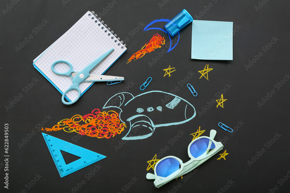 Creative composition with drawn rockets, eyeglasses and different stationery on black chalkboard