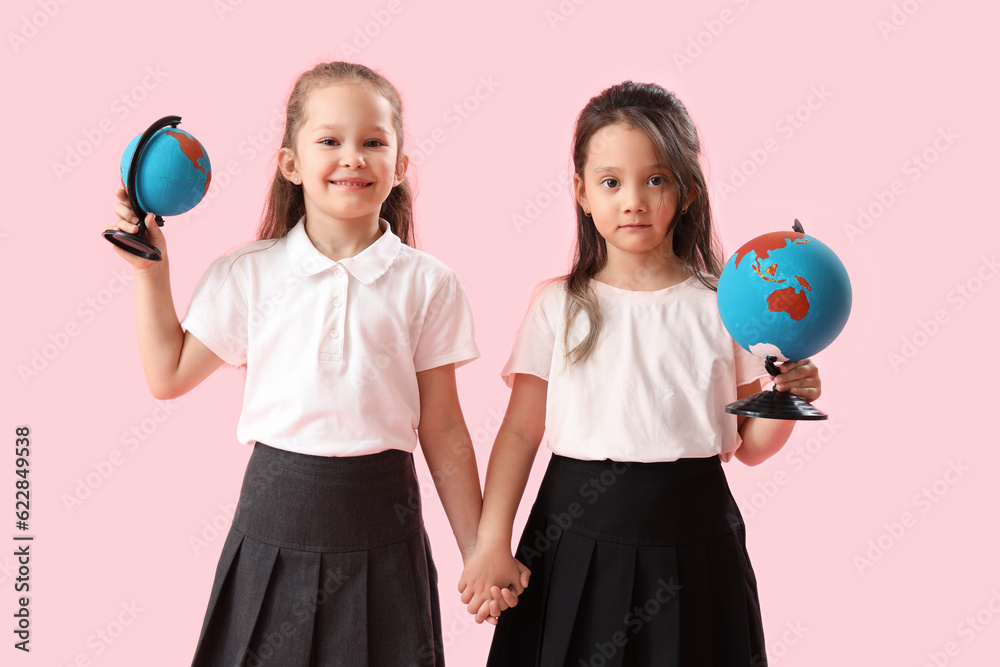 Little schoolgirls with globes on pink background