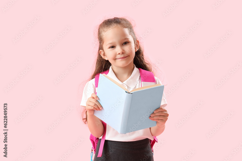 Little schoolgirl with book on pink background