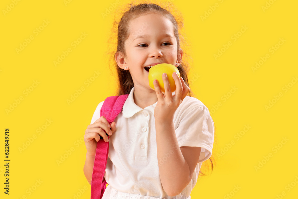 Little schoolgirl with apple on  yellow background