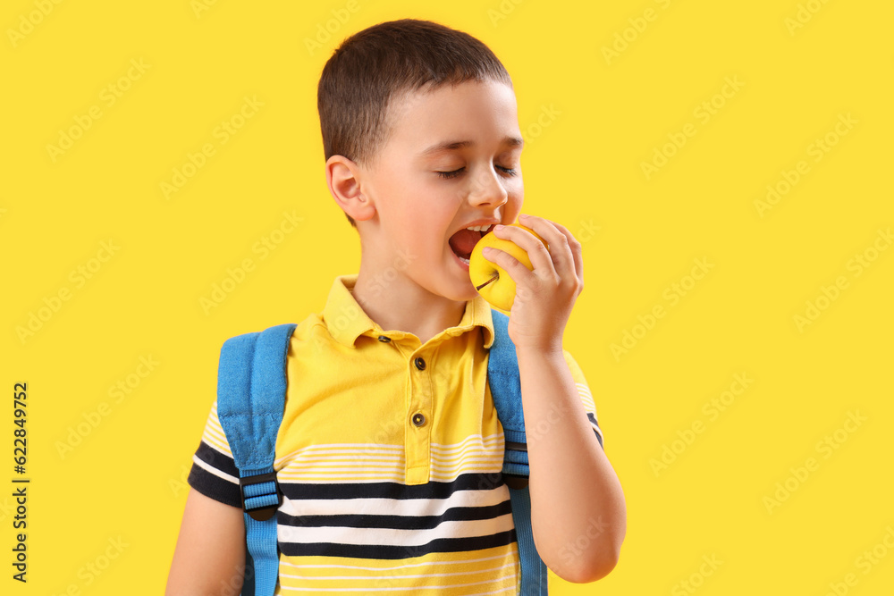 Little schoolboy eating apple on yellow background