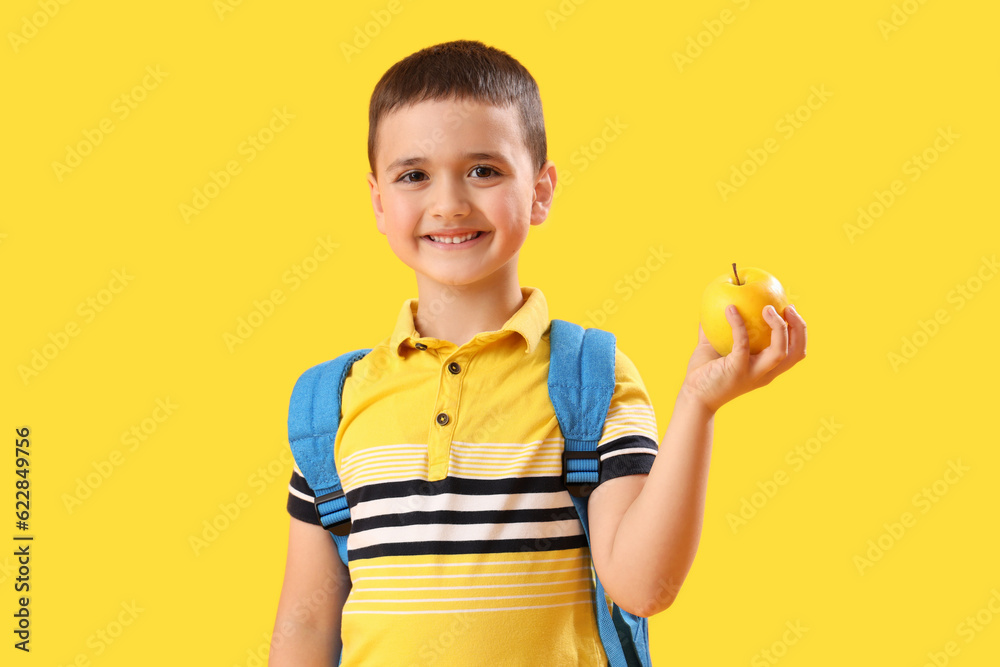 Little schoolboy with apple on yellow background