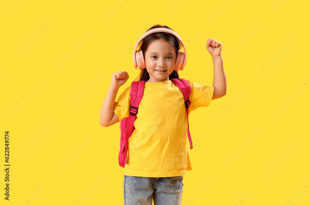 Little schoolgirl listening to music on yellow background