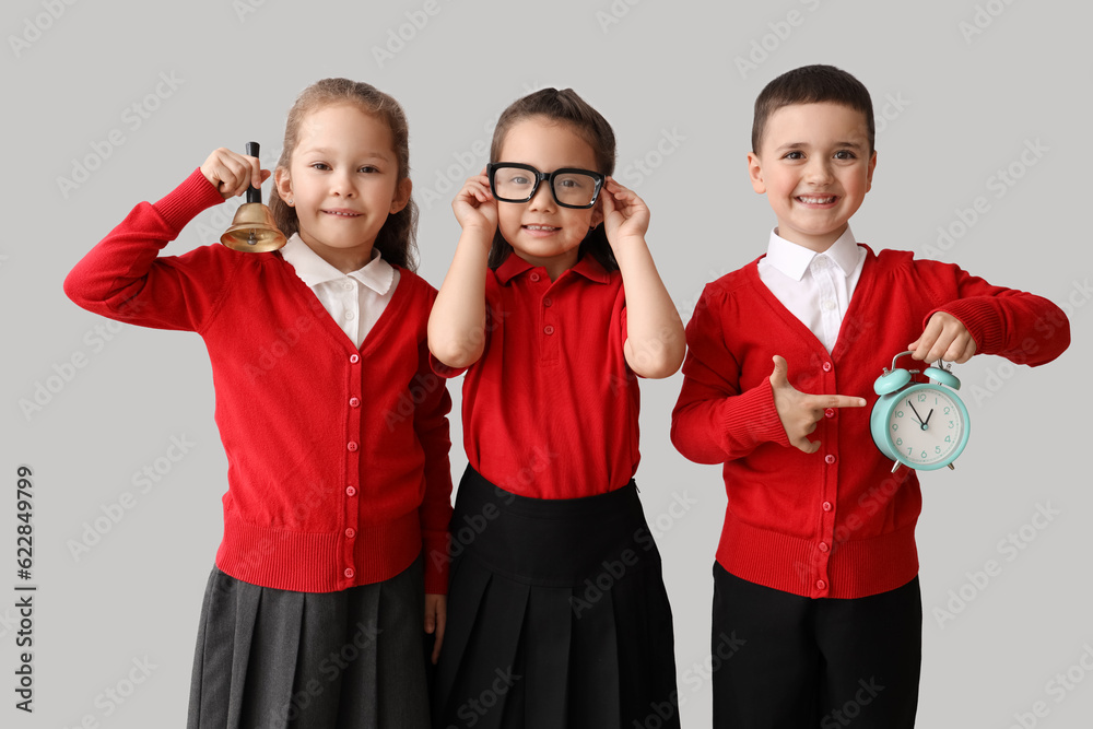 Little schoolchildren with bell and alarm clock on grey background