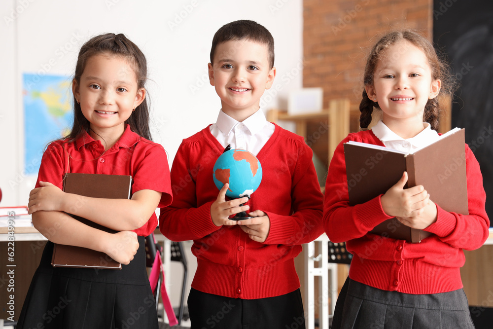 Little schoolchildren with globe and books in classroom