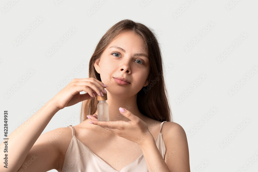 Pretty young woman with cosmetic oil on light background