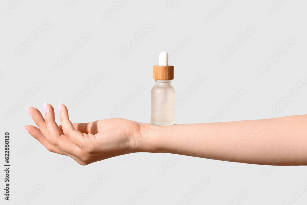 Hand of woman with bottle of cosmetic oil on light background