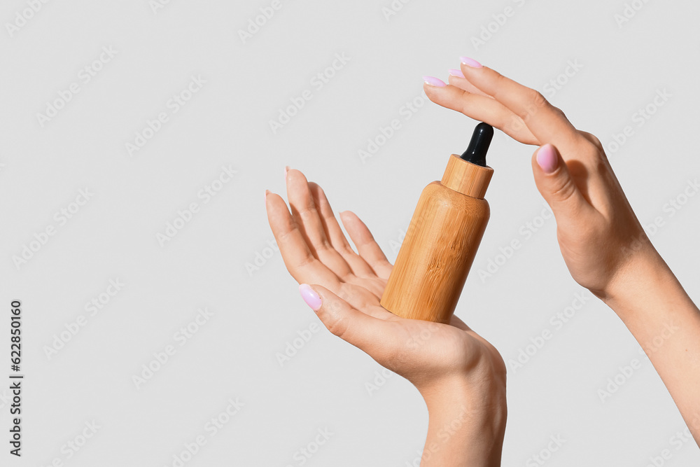 Hands of woman with bottle of cosmetic oil on light background