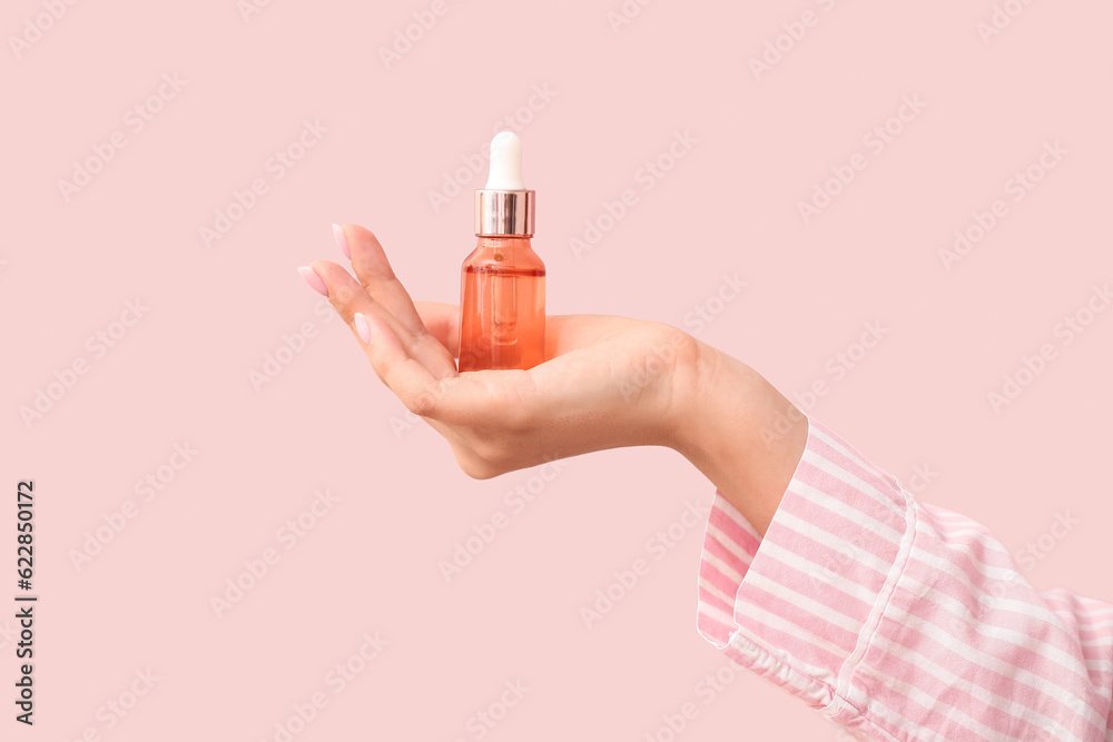 Hand of woman with bottle of cosmetic oil on pink background