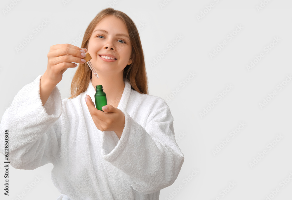 Pretty young woman with cosmetic oil on light background