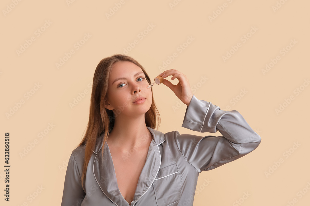 Pretty young woman with cosmetic oil on beige background