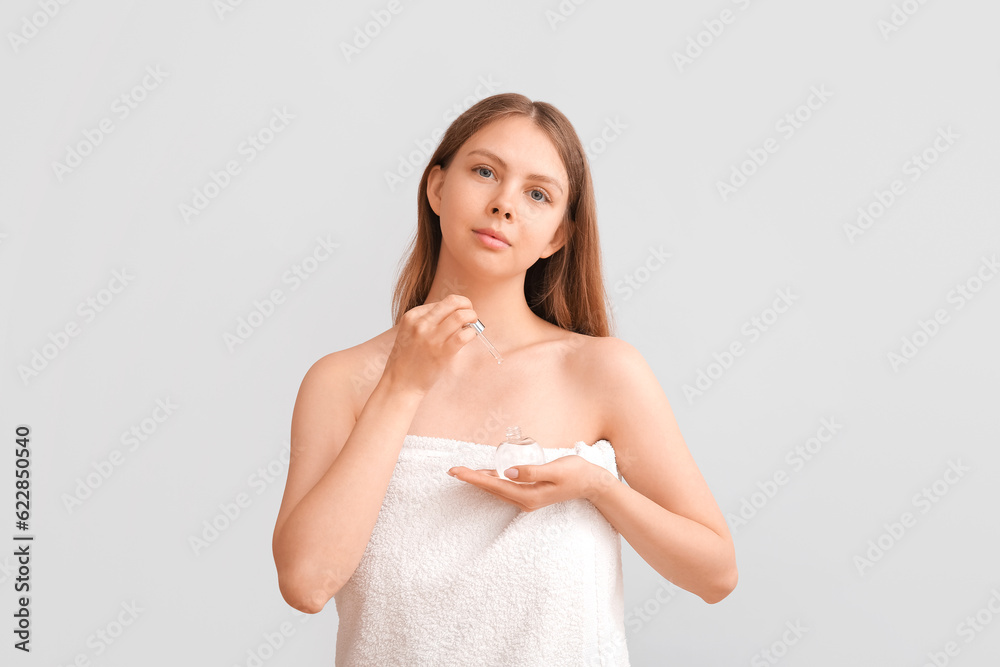 Pretty young woman with cosmetic oil on light background