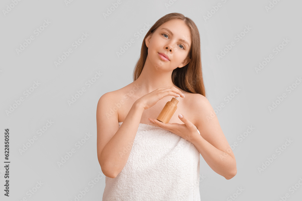 Pretty young woman with cosmetic oil on light background