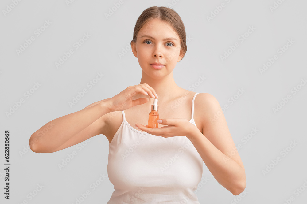 Pretty young woman with cosmetic oil on light background