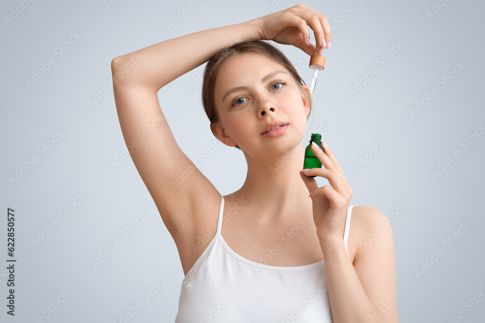 Pretty young woman with cosmetic oil on light background