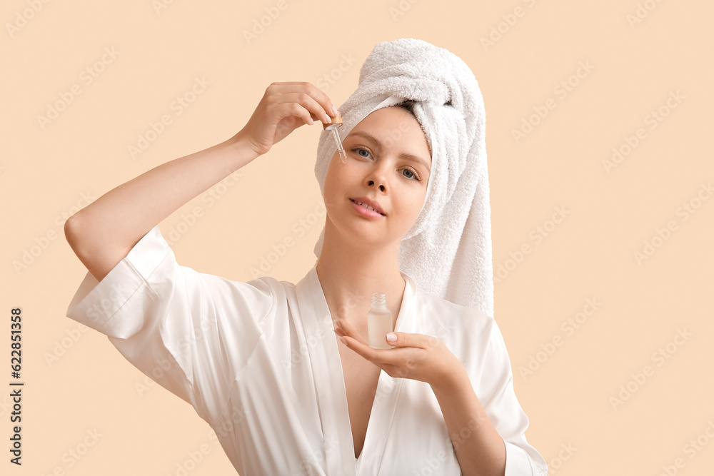 Pretty young woman with cosmetic oil on beige background