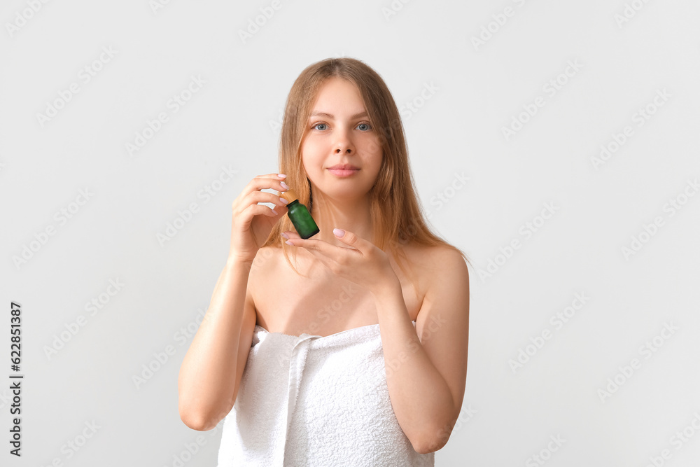 Pretty young woman with cosmetic oil on light background