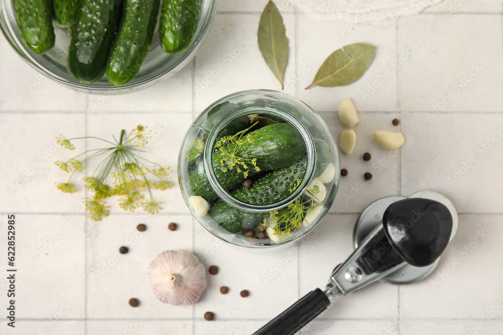 Jar with fresh cucumbers for preservation on white tile background