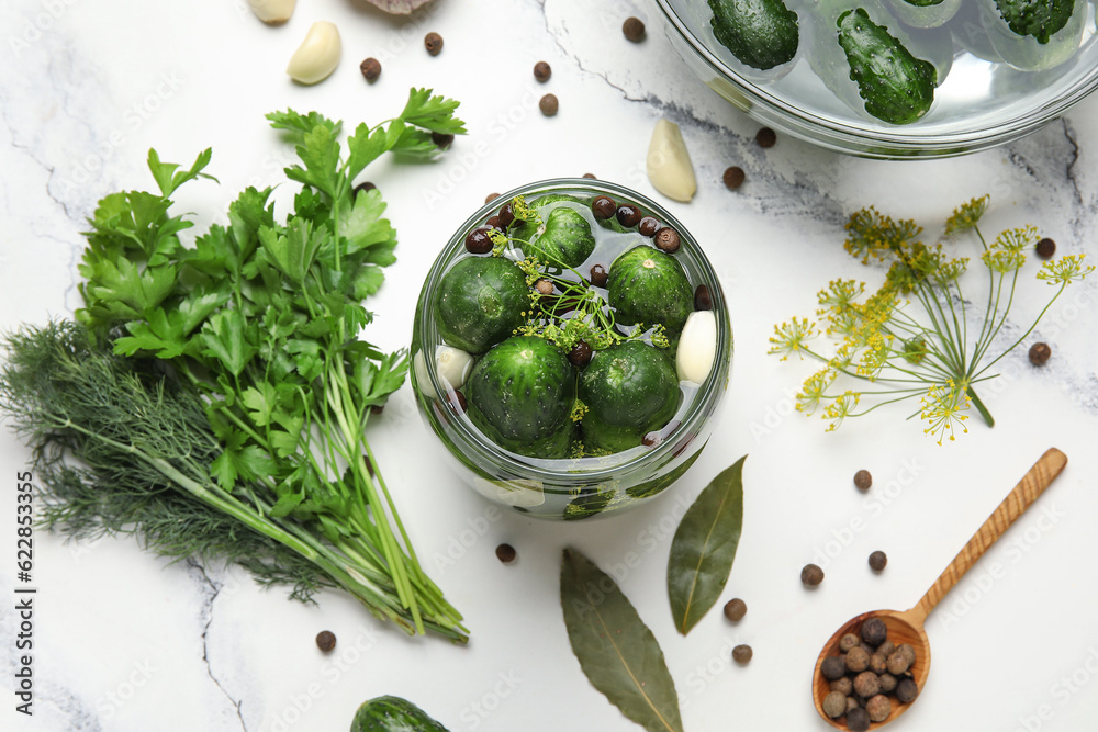 Jar with fresh cucumbers and ingredients for preservation on white marble background