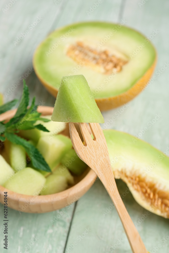 Half of sweet melon and bowl with pieces on green wooden background