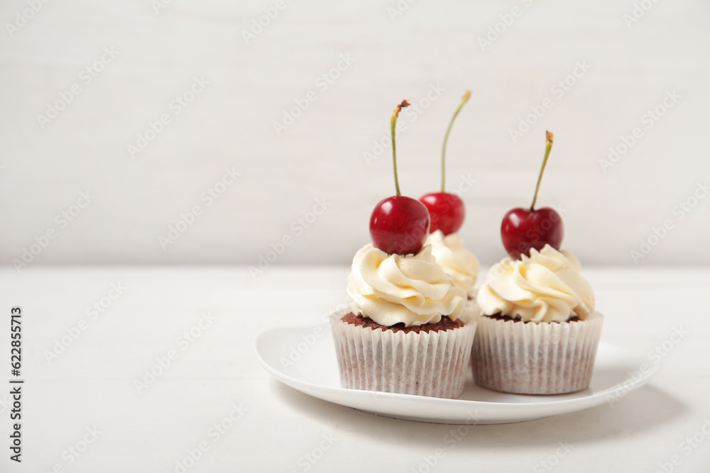 Plate with tasty cherry cupcakes on table