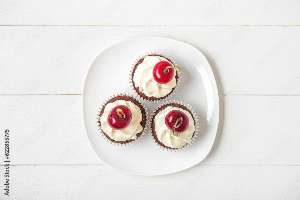 Plate with tasty cherry cupcakes on white wooden background