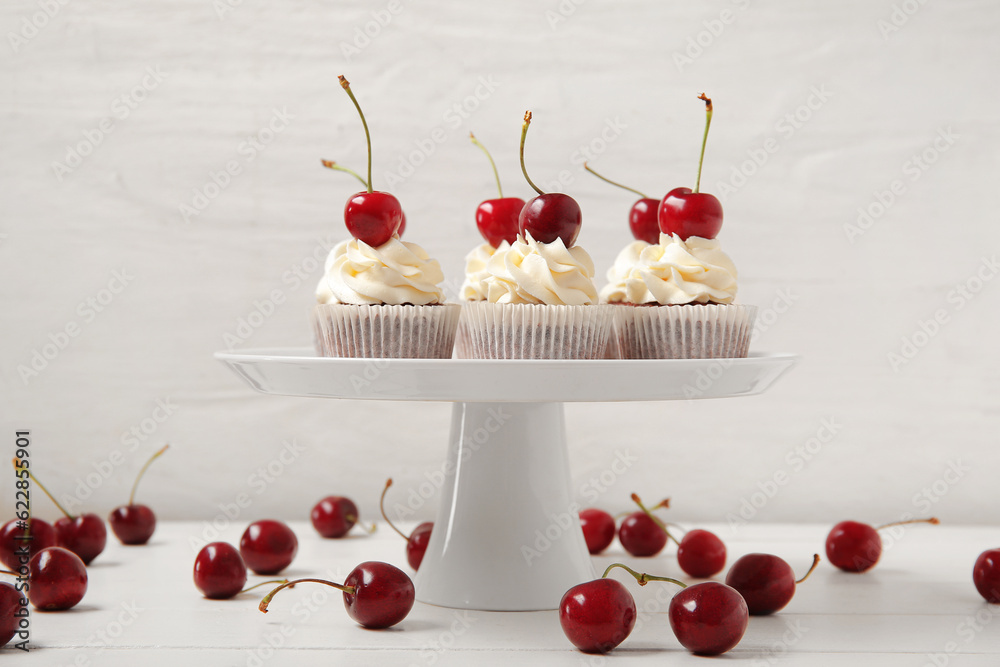 Stand with tasty cherry cupcakes on table