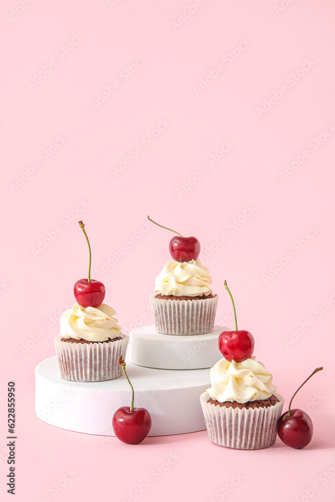 Decorative stand with tasty cherry cupcakes on pink background