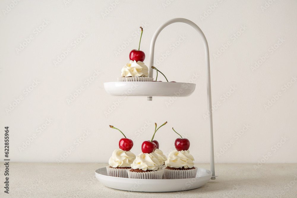 Stand with tasty cherry cupcakes on light background