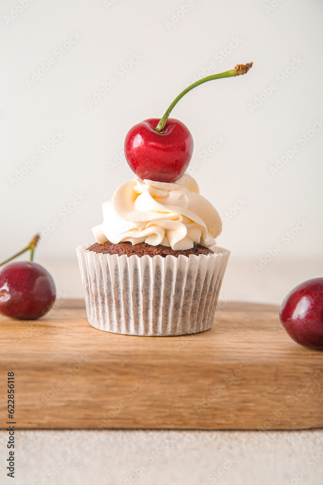 Wooden board with tasty cherry cupcake on light background