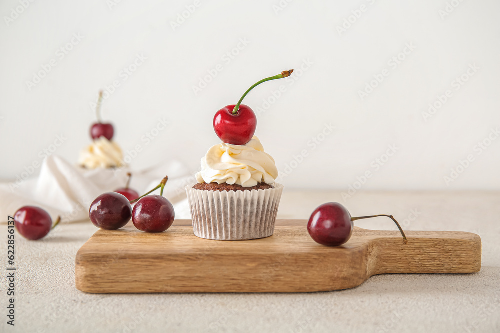 Wooden board with tasty cherry cupcake on light background