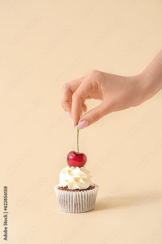 Woman decorating tasty cupcake with cherry on beige background