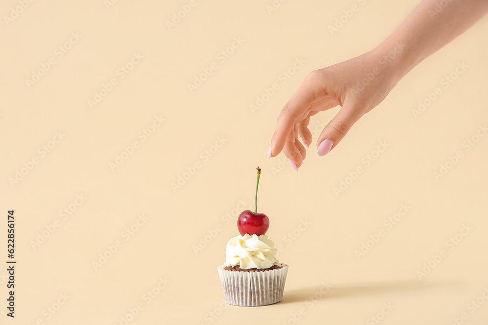 Woman decorating tasty cupcake with cherry on beige background