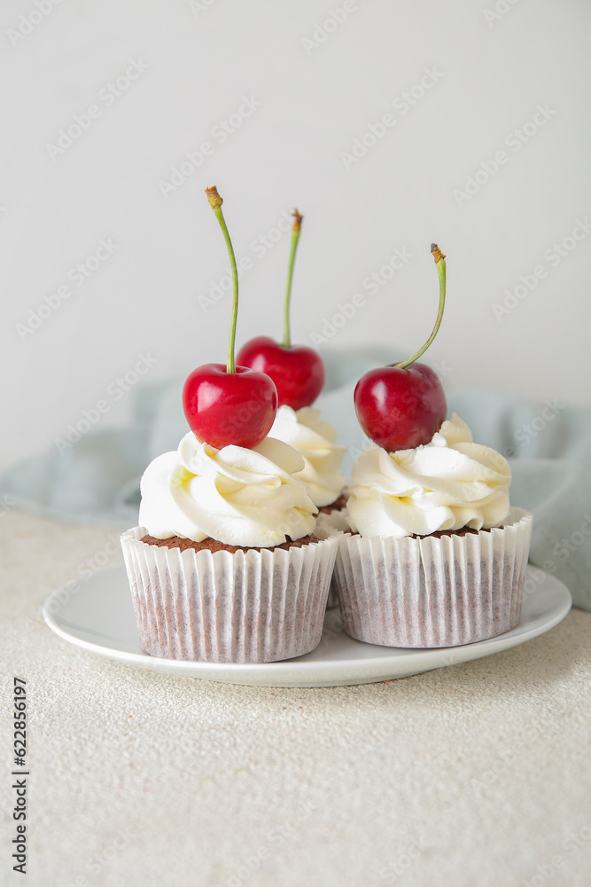 Plate with tasty cherry cupcakes on light background