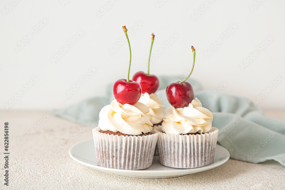 Plate with tasty cherry cupcakes on light background