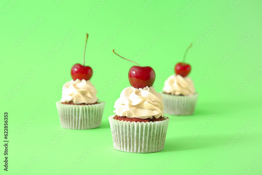 Tasty cherry cupcakes on green background