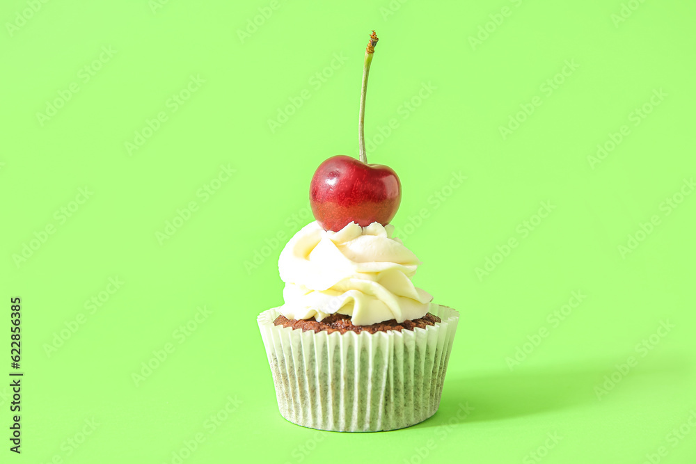 Tasty cherry cupcake on green background