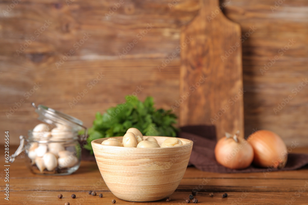 Bowl with canned mushrooms on wooden background