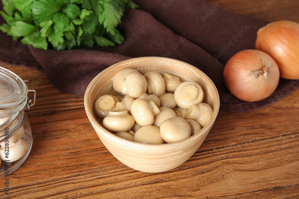 Bowl with canned mushrooms on wooden background