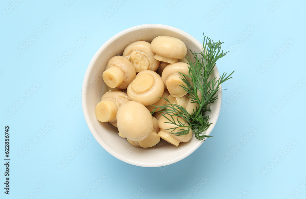 Bowl with canned mushrooms on blue background